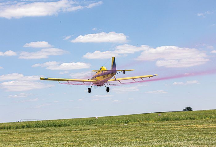 An airplane flies over a field of young crops applying an aerial spray of crop inputs