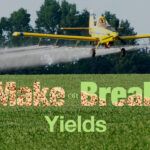 A plane making an aerial fungicide application to a field with the Make or Break Yields text